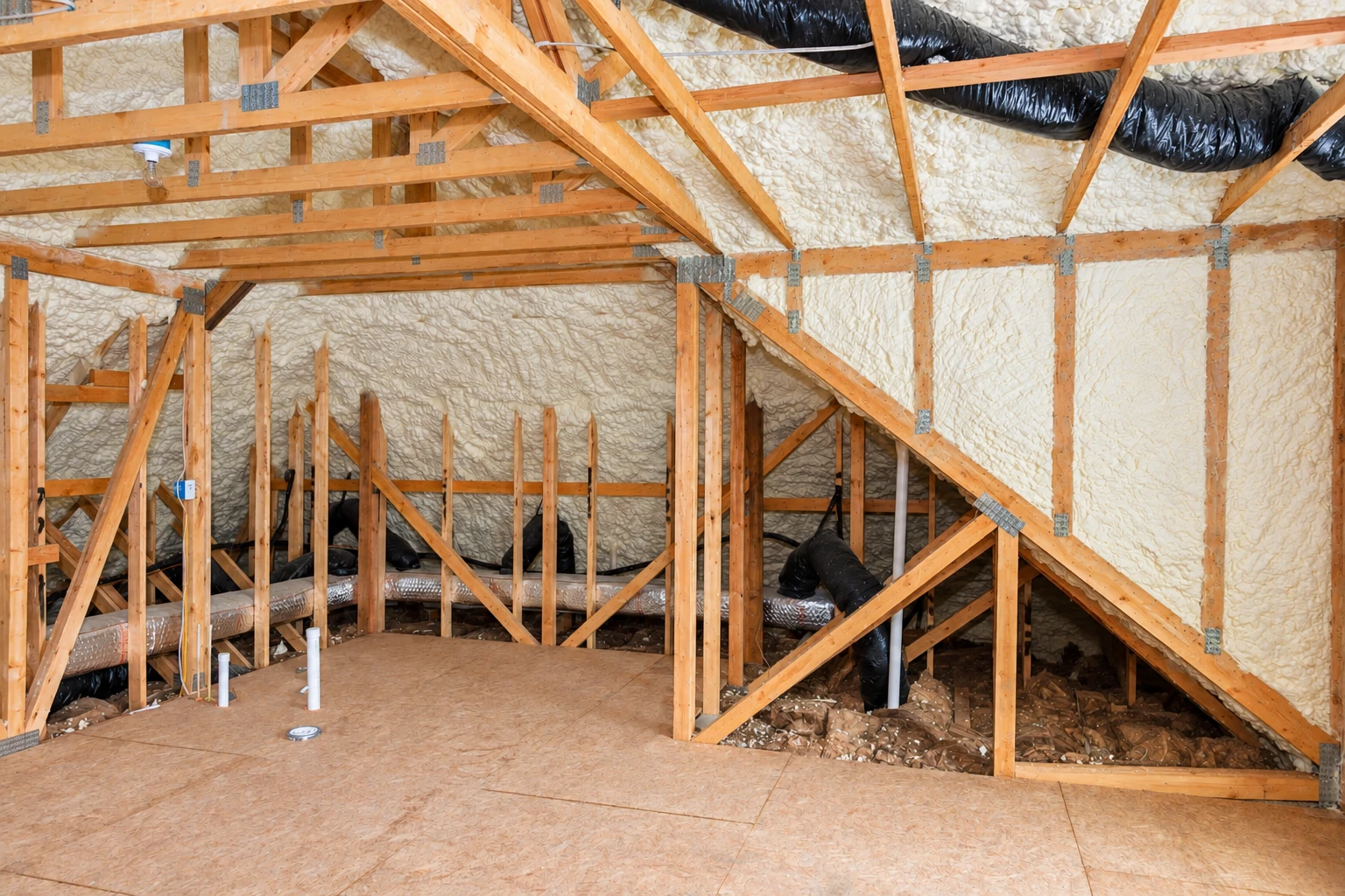 Exposed attic rafters and roof cavities are covered with white spray foam, with black ventilation ducts and pipes below.