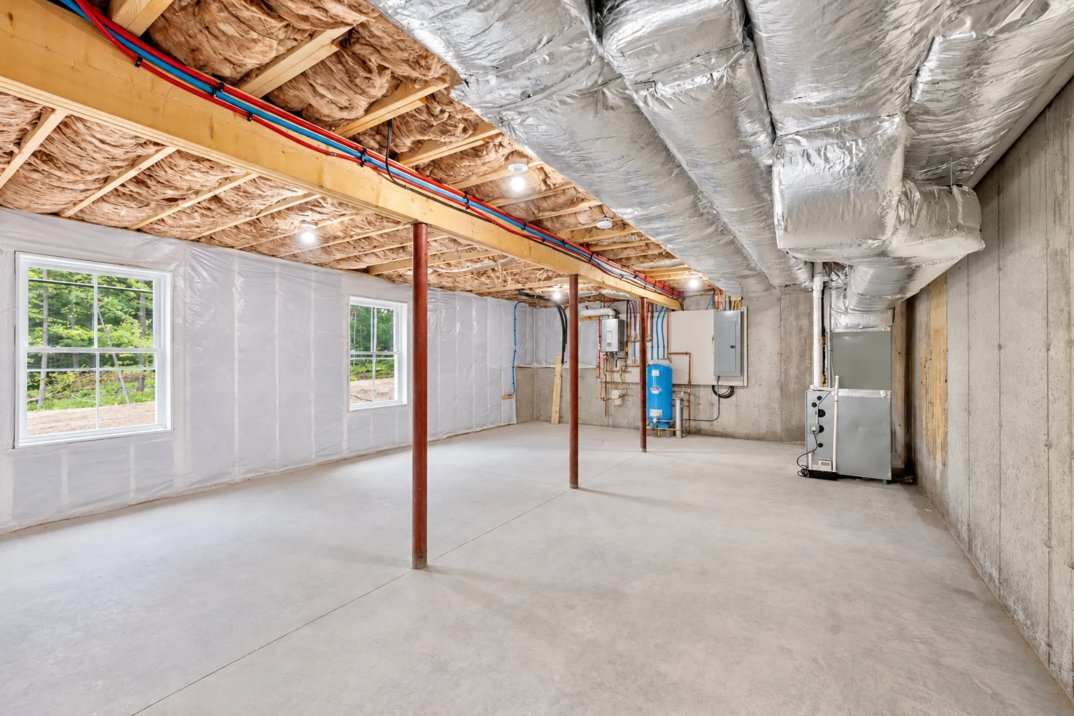 A basement has insulated walls and ceiling, exposed ductwork, windows, and utility equipment.