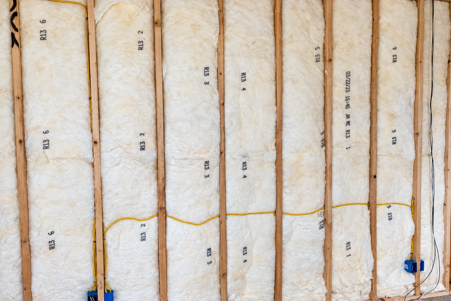 Fiberglass batts marked R-13 fill wall cavities between exposed wooden studs, with yellow wiring running across them.