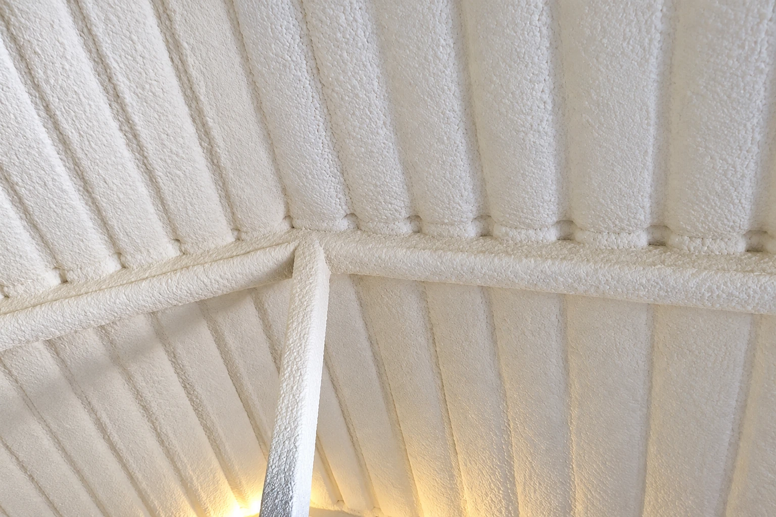 Thick white spray foam coats the underside of a roof, covering the rafters and a crossbeam.